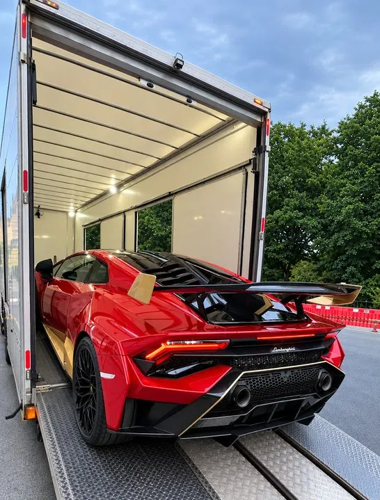 Red Lamborghini being loaded into an enclosed car transport trailer.